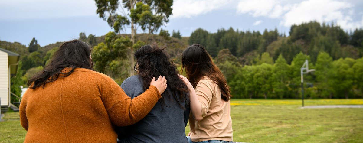 Three women of Pacific descent hugging in solidarity, emphasising communal support against family violence
