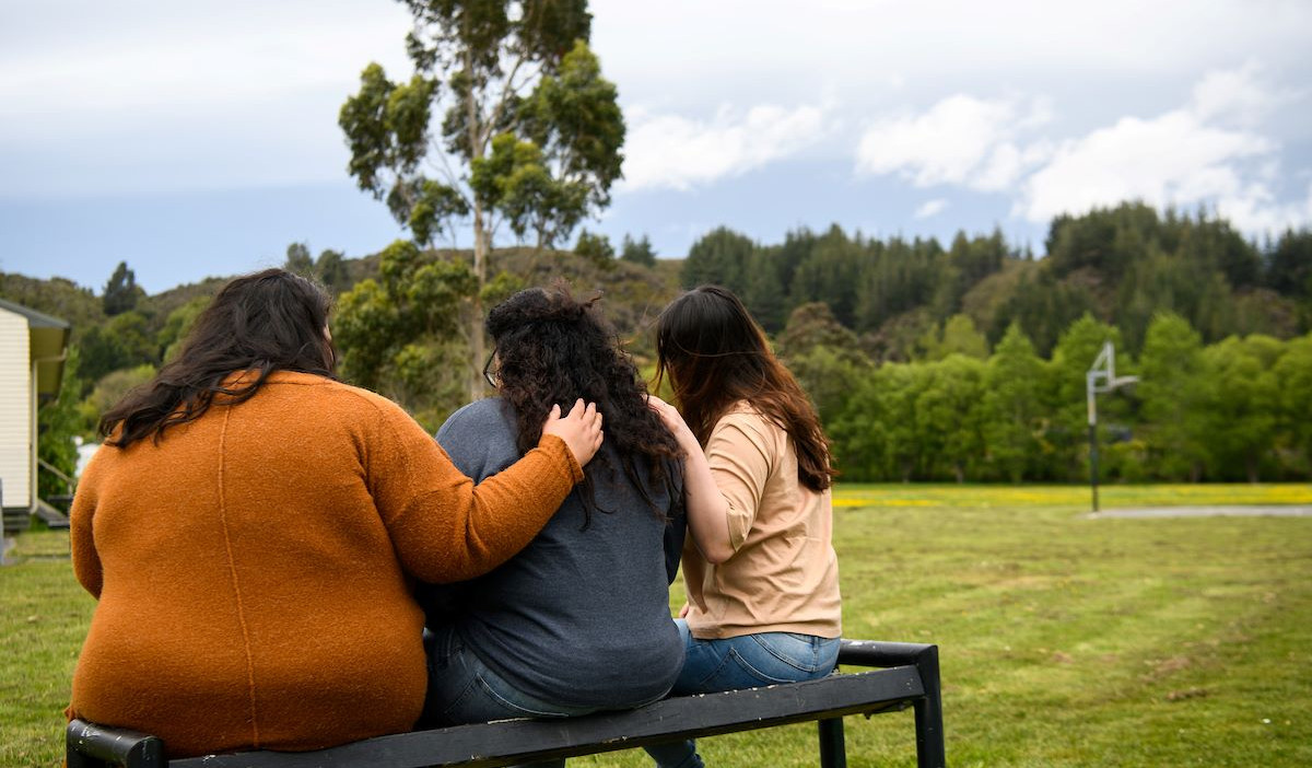 Three women of Pacific descent hugging in solidarity, emphasising communal support against family violence