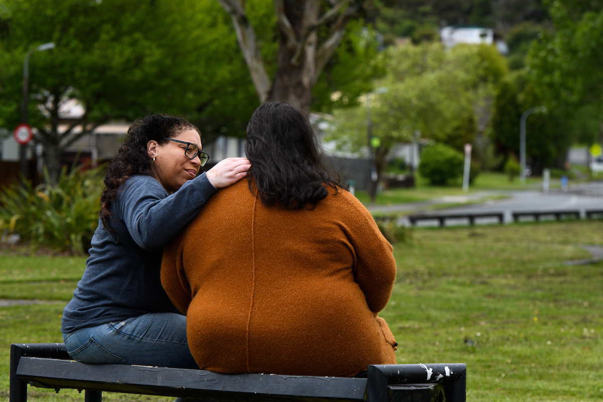 Two women sitting on a doorstep, having a supportive conversation about self-care while helping others with family violence issues