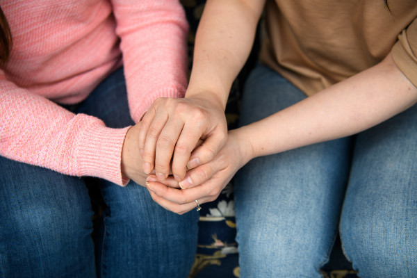 Close up of two people sitting on a couch and clasping hands.